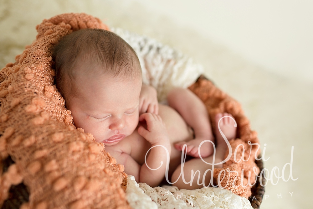 newborn baby girl curled up inside a basket